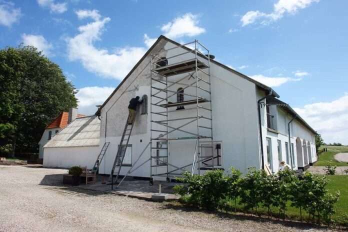 Man on scaffolds painting a house